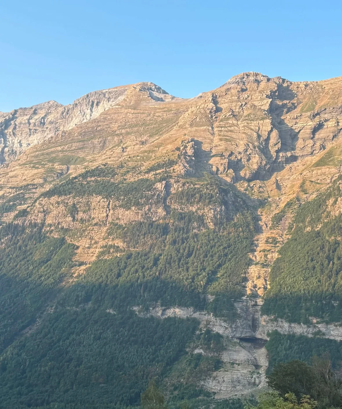 Sluncem osvětlená skalní stěna nad zeleným údolím v Pyrenejích