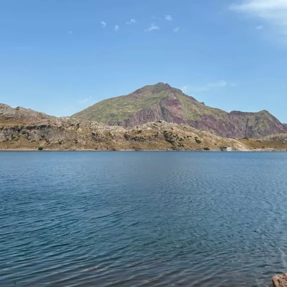 Modré horské jezero s travnatými a skalnatými vrcholy za slunečného dne