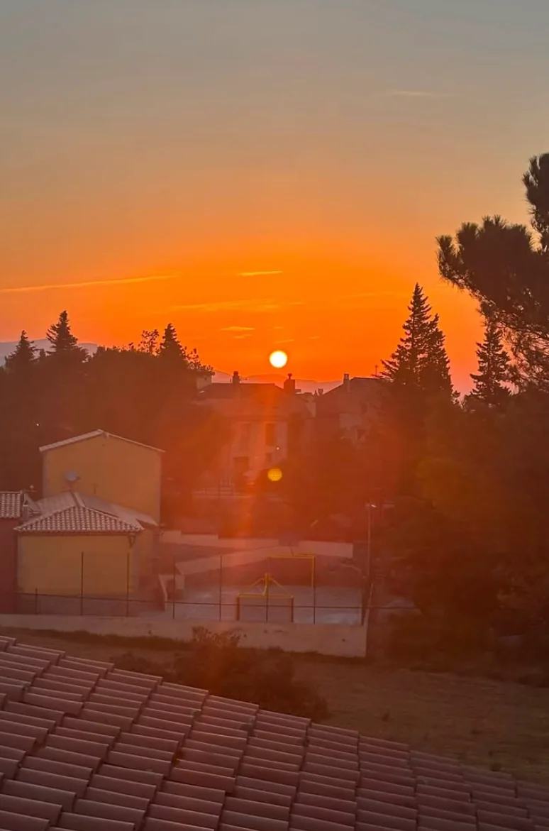 Oranžový východ slunce nad střechami domů a siluetami stromů